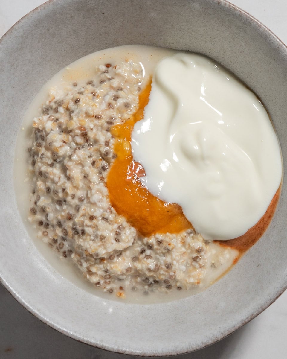 Overnight oats in a bowl with fruit puree, yogurt and almond butter added on top.