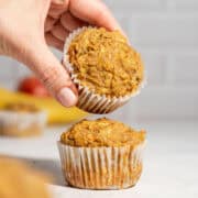 Two apple banana carrot muffins on a table with one muffin being held above the other to show the soft texture.