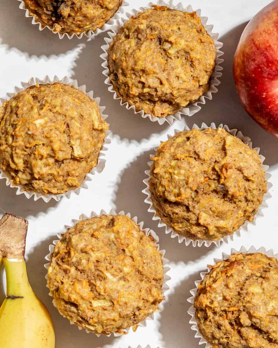 Birds-eye-view of 6 apple banana carrot muffins, next to it 1 apple and 1 banana.