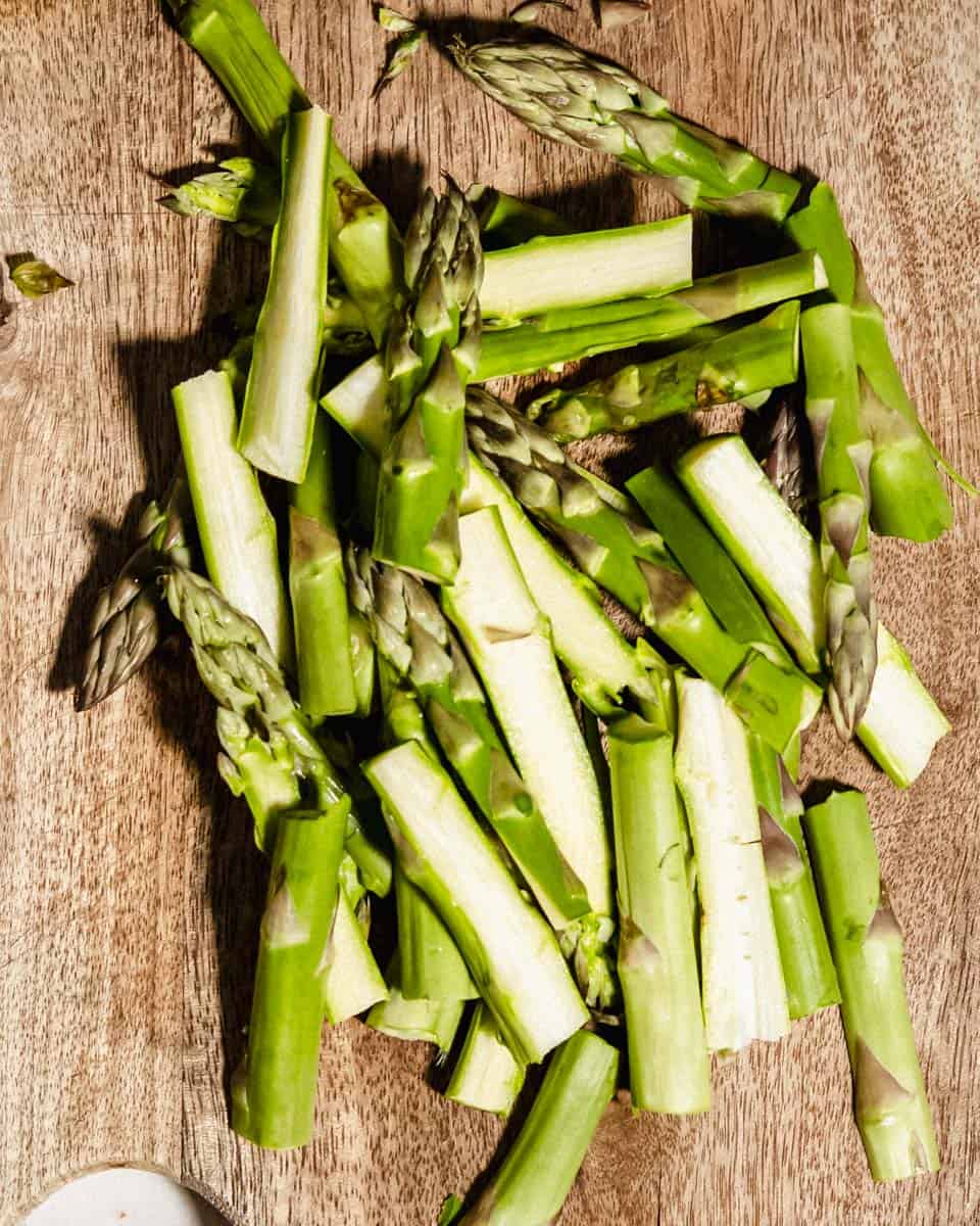 Asparagus chopped in half lenghtwise on a cutting board.