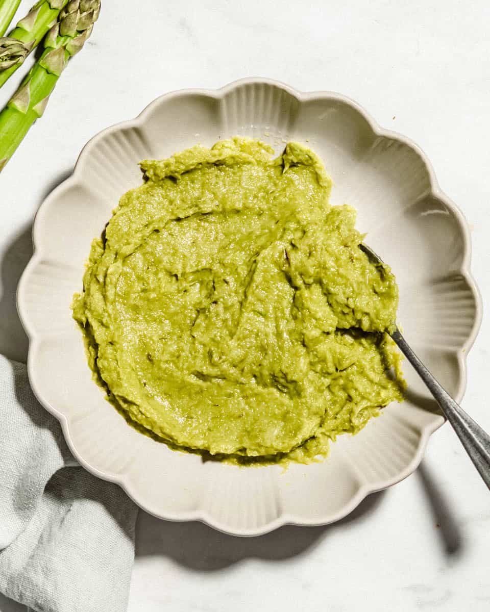 Asparagus puree on a plate next to it some fresh asparagus.