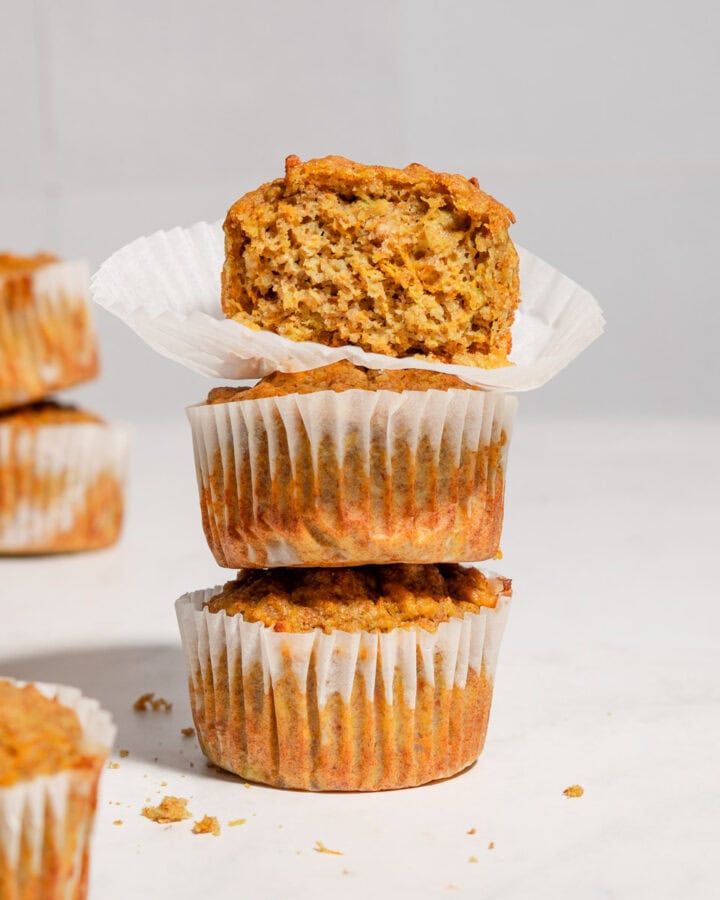 A stack of 3 carrot banana zucchini muffins with the upper one showing the texture inside.