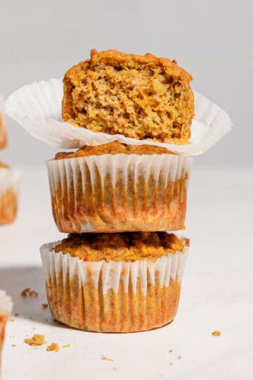 A stack of 3 carrot banana zucchini muffins with the upper one showing the texture inside.