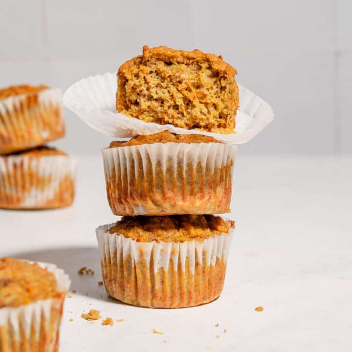 A stack of 3 carrot banana zucchini muffins with the upper one showing the texture inside.