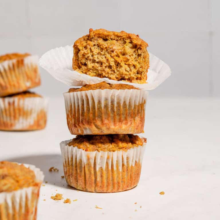 A stack of 3 carrot banana zucchini muffins with the upper one showing the texture inside.