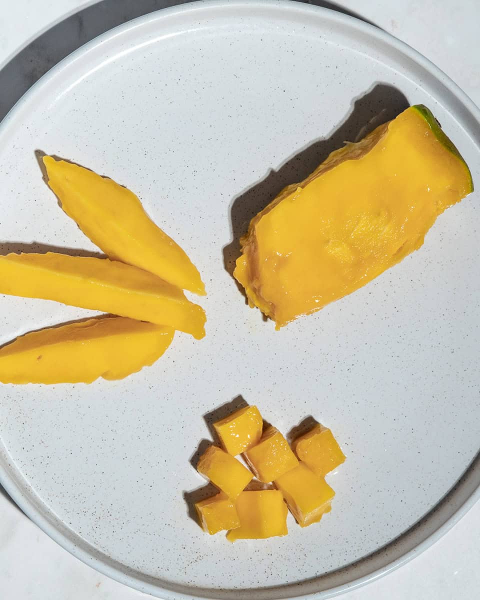 Mango pit with most of the flesh removed, mango spears and bite-sized mango pieces on a plate.