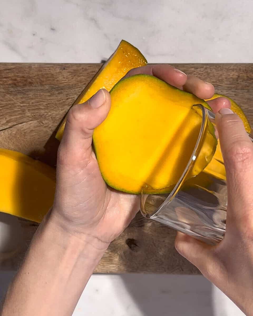 Mango flesh being scooped out with a whiskey glass.