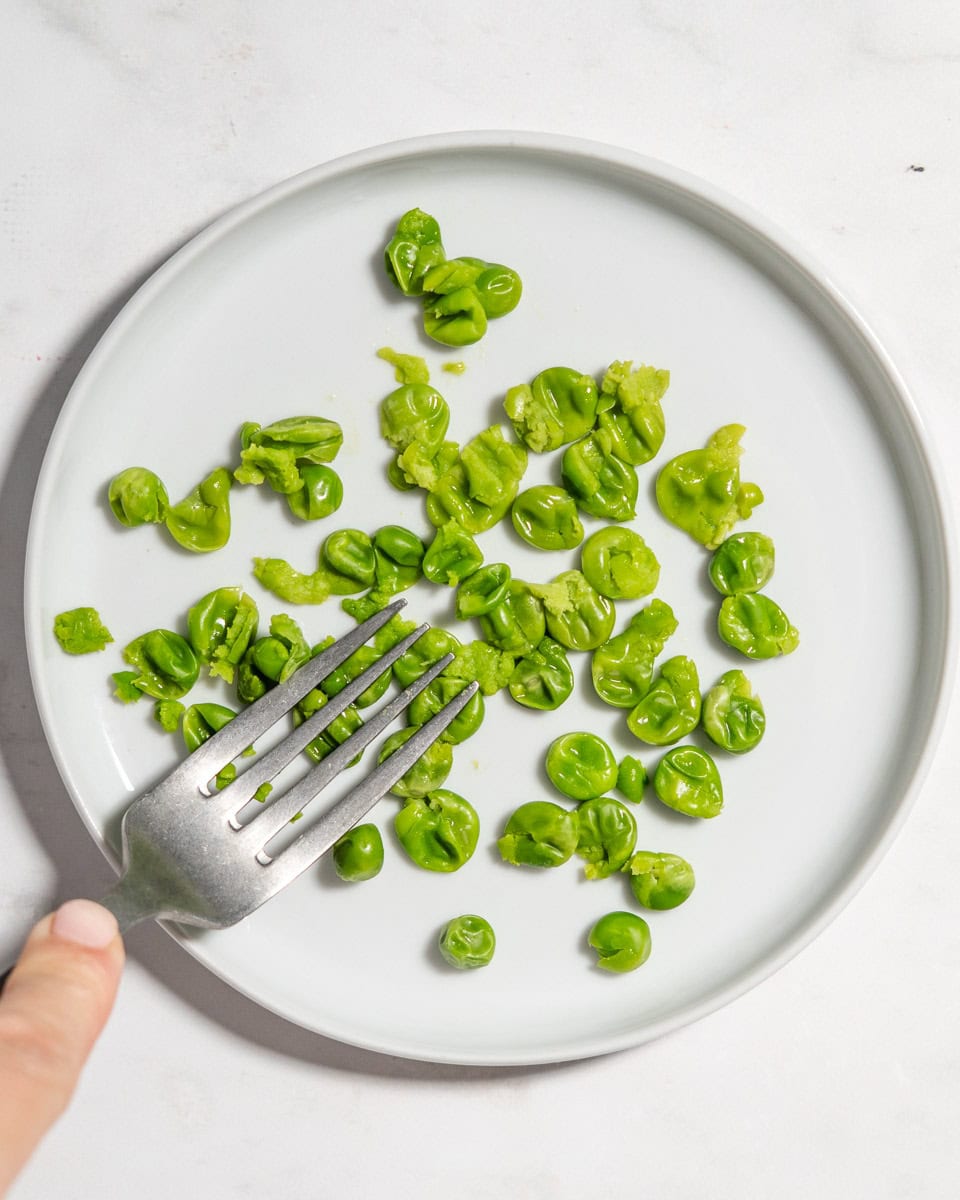 Cooked peas being mashed with a fork.