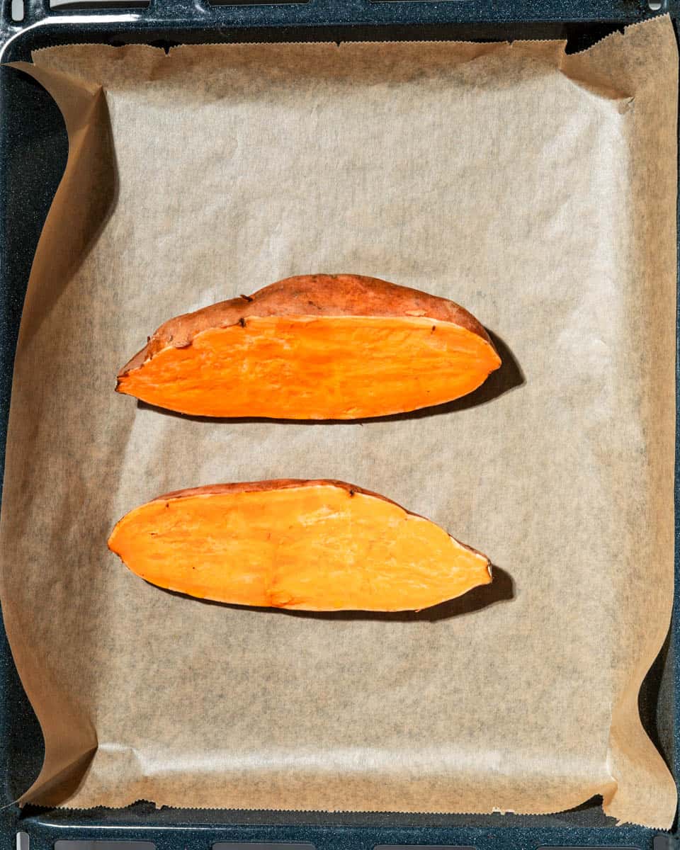 Sweet potato cut lengthwise on a parchment paper lined baking sheet.