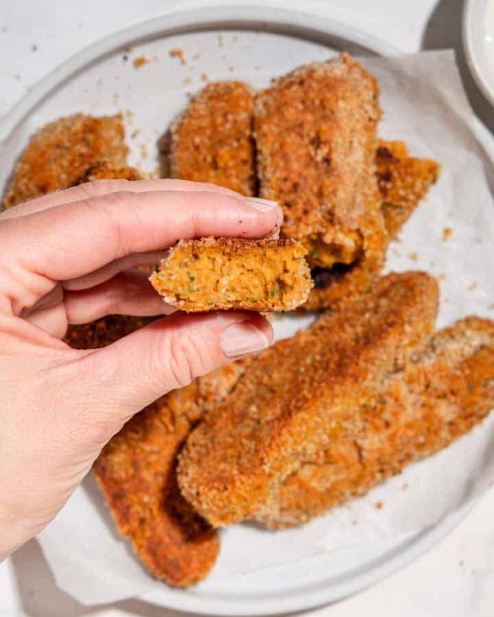 sweet potato nuggets served on a plate, with one nugget held up close to the camera showing a bite taken out of the soft orange center.