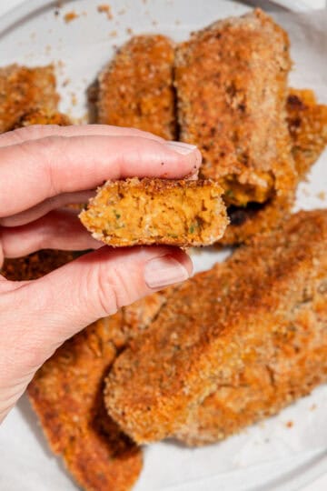 sweet potato nuggets served on a plate, with one nugget held up close to the camera showing a bite taken out of the soft orange center.