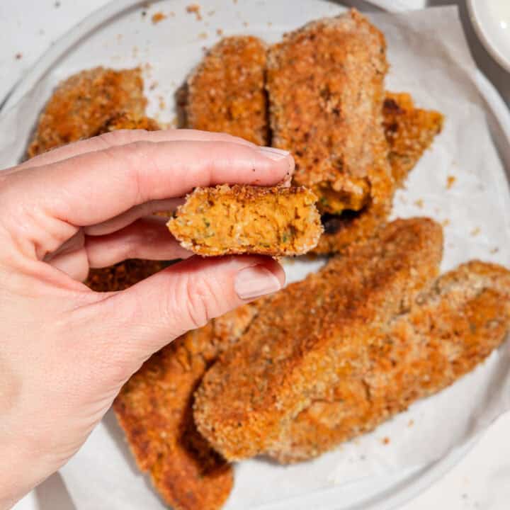 sweet potato nuggets served on a plate, with one nugget held up close to the camera showing a bite taken out of the soft orange center.